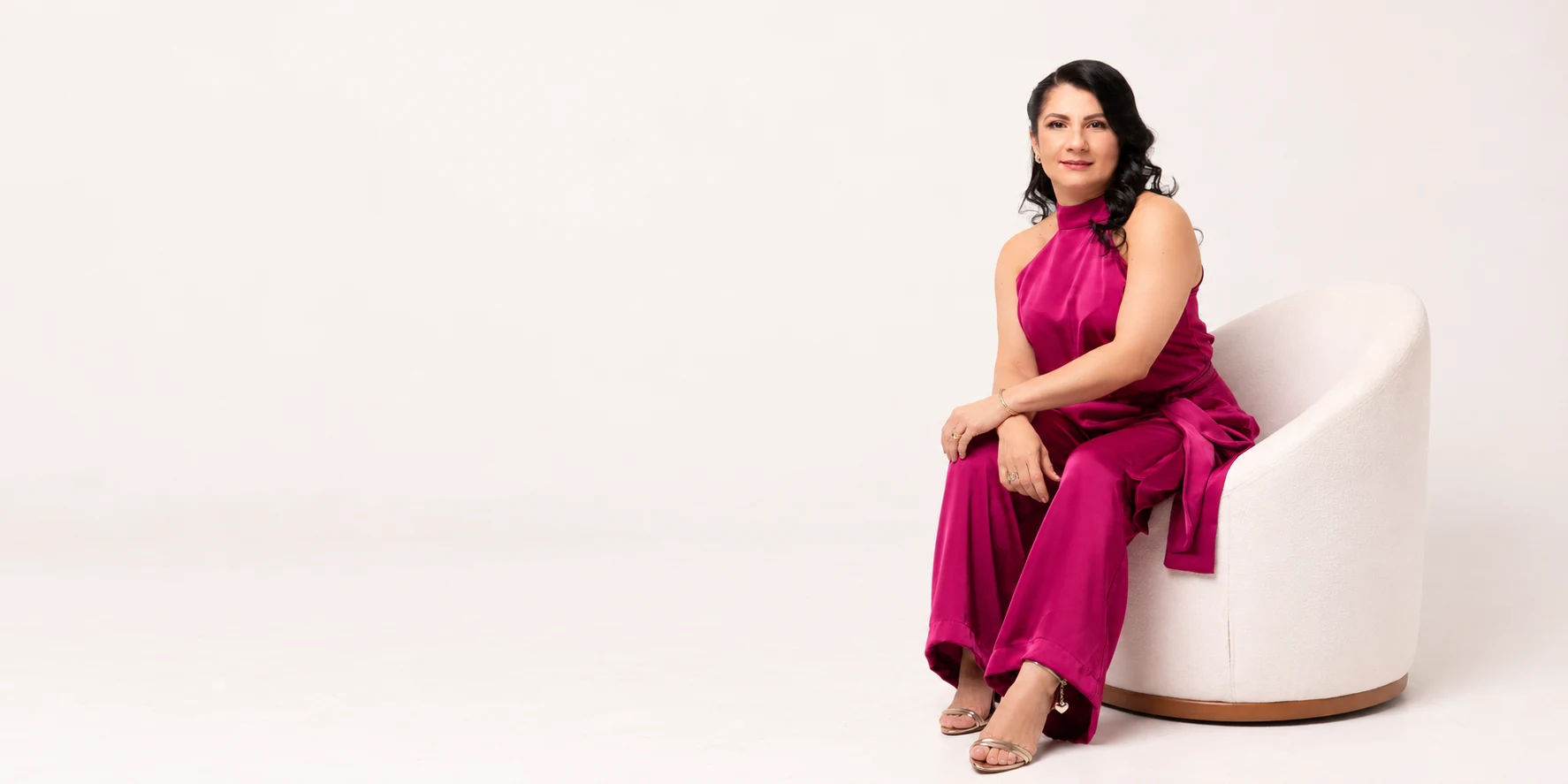 Dra. Denise Menezes, sentada em uma poltrona, com roupa magenta